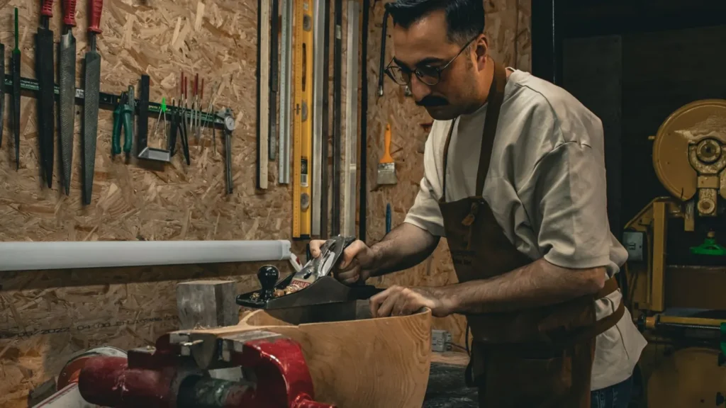 Menuisier qui rabote une pièce de bois à l’établi